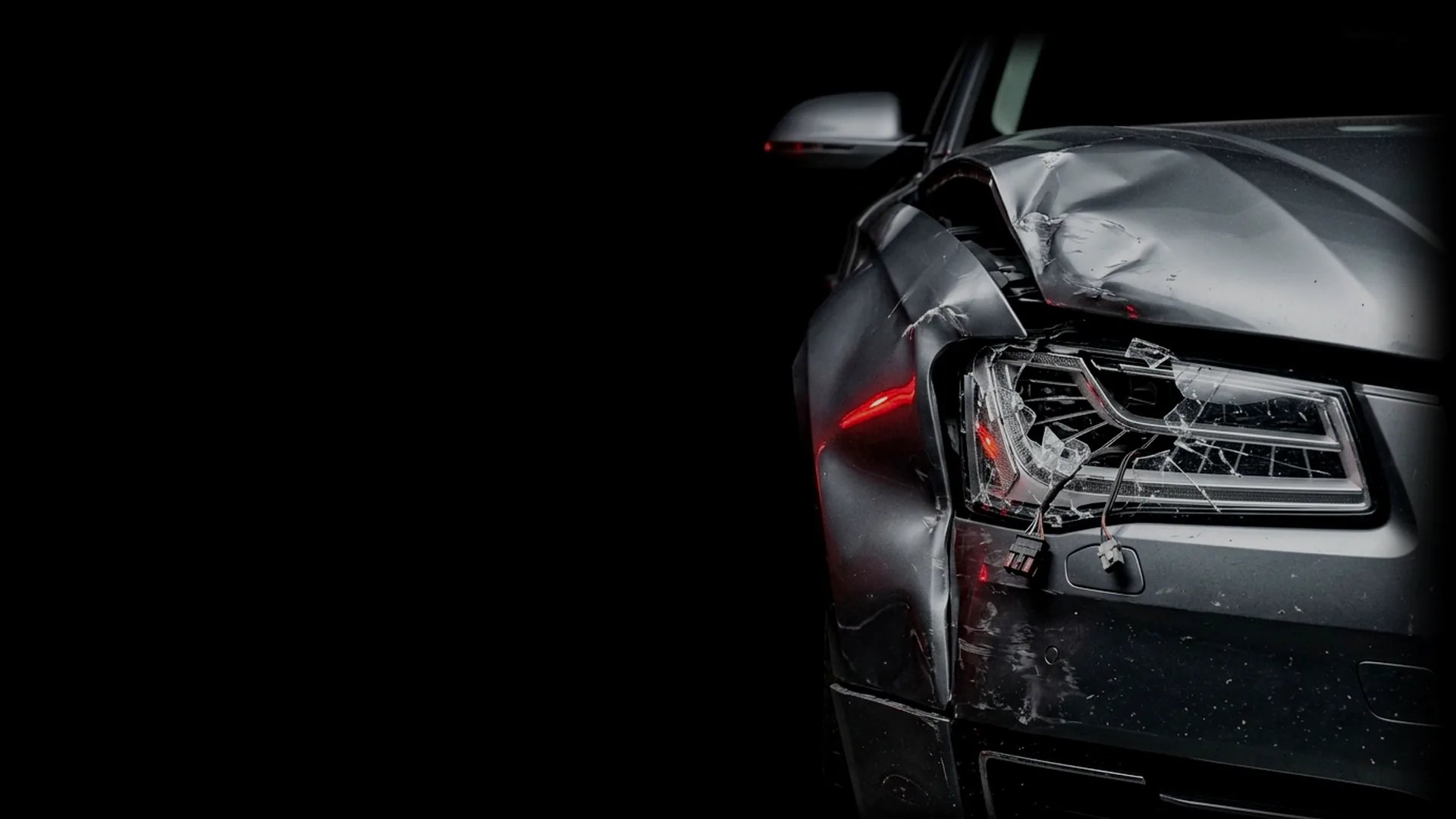 Frente de un auto oscuro chocado, con la óptica rota
